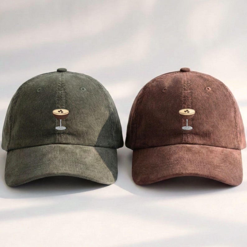 May include: Two corduroy baseball caps, one olive green and one brown. Each cap features an embroidered cocktail glass design. The caps have a curved brim and a button on top, suitable for casual wear.