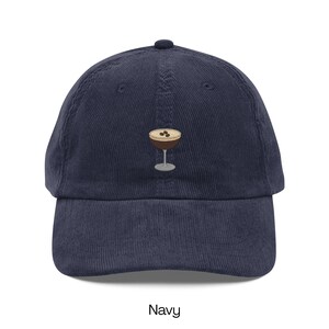 May include: Navy blue corduroy baseball cap with an embroidered cocktail glass design. The cocktail glass has a brown drink with three coffee beans on top. The word "Navy" is printed at the bottom of the image.