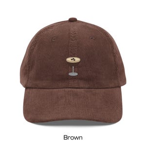 May include: Brown corduroy baseball cap featuring an embroidered cocktail glass design. The cap has a curved brim and an adjustable strap. The word "Brown" is printed at the bottom of the image.