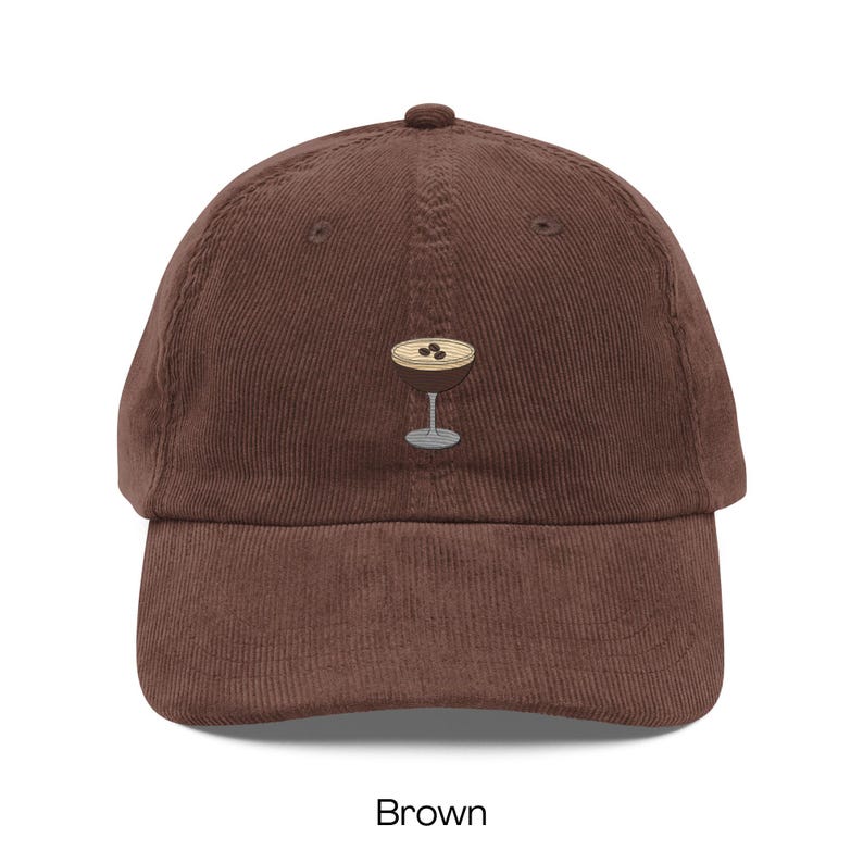 May include: Brown corduroy baseball cap featuring an embroidered cocktail glass design. The cap has a curved brim and an adjustable strap. The word "Brown" is printed at the bottom of the image.