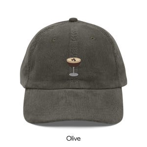 May include: Olive green corduroy baseball cap featuring an embroidered cocktail glass with three coffee beans. The cap has a curved brim and a top button. The word "Olive" is printed at the bottom of the image.