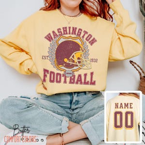 May include: Yellow sweatshirt with a vintage-style Washington Football team logo. The logo features a maroon helmet with a white facemask and the text "Washington Football Est. 1932".