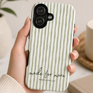 May include: A white and green striped phone case with the text "made for more" and "Ephesians 2:10" in black script. The case has a black border and is held in a person's hand. A white mug and a book are in the background.