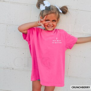 May include: A bright pink t-shirt with the text "HIS WAY IS BETTER" and a cross graphic. The shirt is a vibrant color and is likely made of soft material. The word "CRUNCHBERRY" is in the bottom right corner.