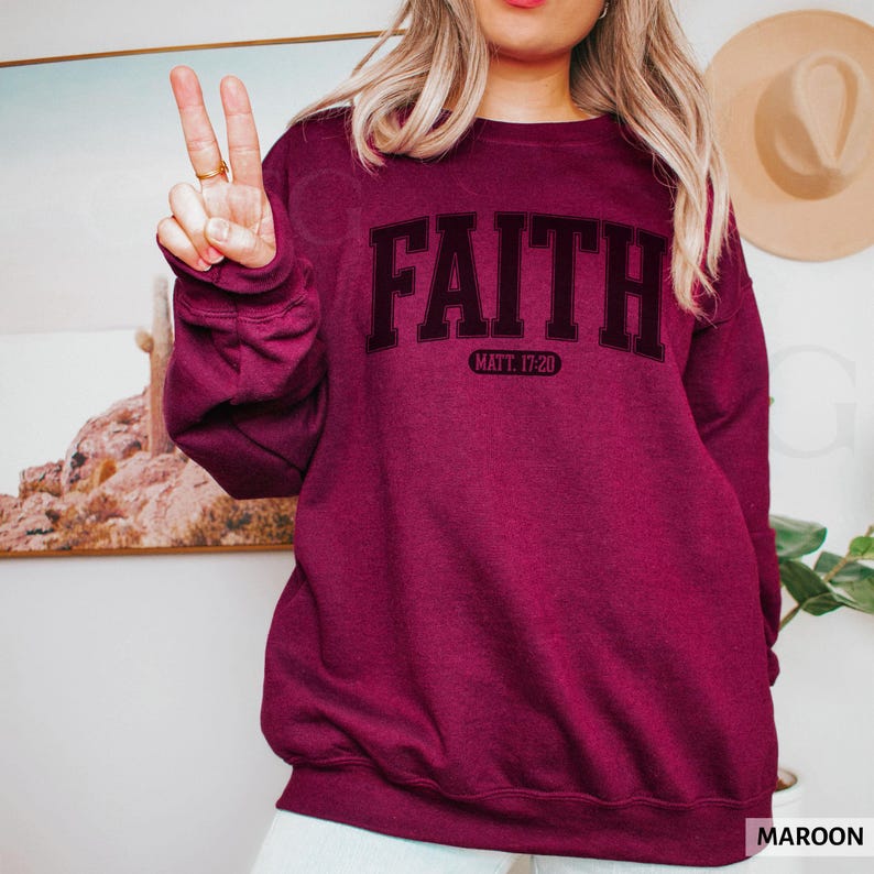 Puede incluir: Sudadera granate con la palabra "FAITH" en negrita, negra, con una fuente de estilo universitario en el pecho. Debajo de la palabra "FAITH" est&aacute; el texto "MATT. 17:20". La sudadera es de color granate liso.