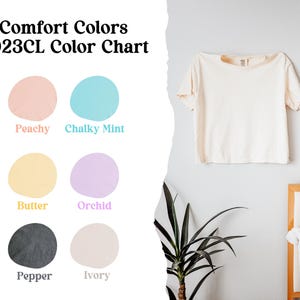 May include: Comfort Colors 3023CL color chart featuring a short-sleeve t-shirt in ivory. The chart displays six circular color swatches labeled Peachy, Chalky Mint, Butter, Orchid, Pepper, and Ivory, showcasing the available fabric color options.