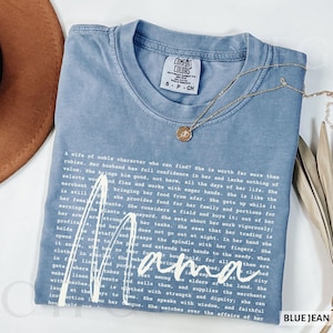 Puede incluir: Camiseta azul vaquero Comfort Colors con la palabra "mama" en escritura blanca. La camiseta presenta un collar de oro y texto de Proverbios 31. La camiseta es talla pequeña.