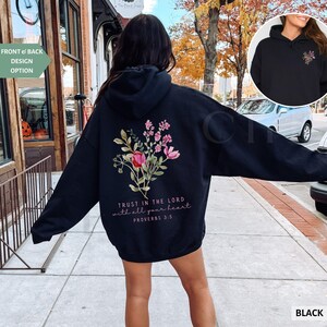 May include: Black hoodie with a floral design on the back, featuring pink and red flowers with green leaves. The text "TRUST IN THE LORD with all your heart PROVERBS 3:5" is printed below the flowers. A smaller image of the hoodie is in the upper right corner.