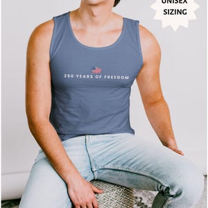 May include: A blue tank top with the text "250 YEARS OF FREEDOM" and a small American flag graphic. The tank top is a solid blue color. The words "UNISEX SIZING" are in a white starburst shape. The words "BLUE JEAN" are in a white rectangle.