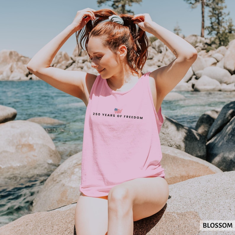May include: A light pink tank top with the text "250 YEARS OF FREEDOM" and a small American flag graphic. The sleeveless top is made of a soft material.