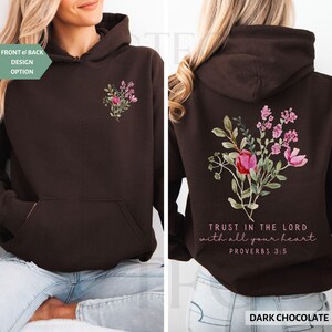May include: Dark chocolate hoodie with a floral design on the front and back. The front features a small bouquet, while the back displays a larger arrangement with the text "TRUST IN THE LORD with all your heart PROVERBS 3:5".