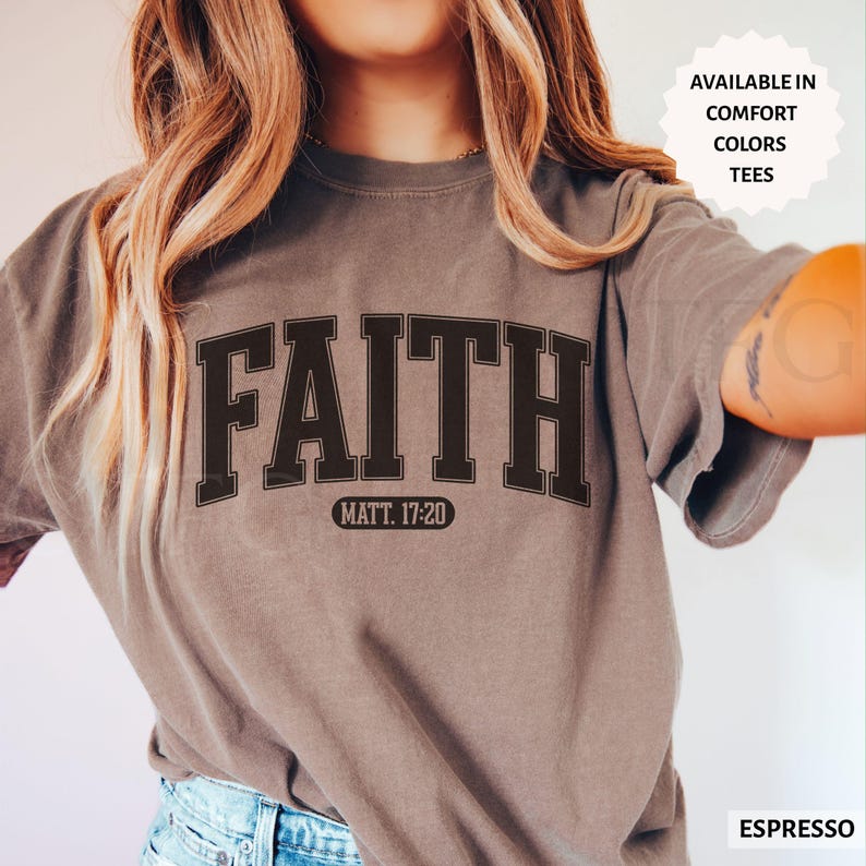 Puede incluir: Camiseta color espresso con la palabra "FAITH" en negrita, marr&oacute;n oscuro, con tipograf&iacute;a universitaria. Debajo, "MATT. 17:20". Disponible en colores confort y camisetas.