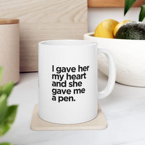 May include: White ceramic coffee mug with black text that reads "I gave her my heart and she gave me a pen."