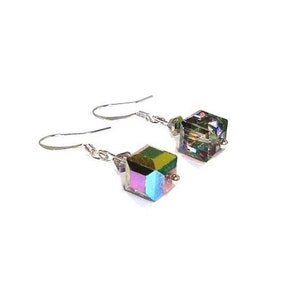 May include: A pair of iridescent cube earrings with silver-colored hooks. The earrings feature a geometric design with a spectrum of colors, including green, purple, and blue, reflecting light. The earrings are set against a white background.