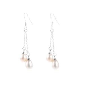 May include: A pair of dangle earrings featuring two white, teardrop-shaped pearls suspended from delicate silver chains. The earrings have a simple hook closure and are set against a white background.