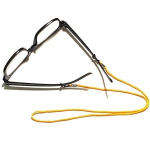 May include: Black framed glasses with a yellow cord attached to the arms. The cord is looped around the arms of the glasses and hangs down.