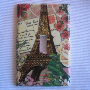 May include: Decorative light switch cover featuring the Eiffel Tower, postcards, and floral accents. The design includes roses and script on a cream background. The cover has a rectangular shape with a single switch opening.