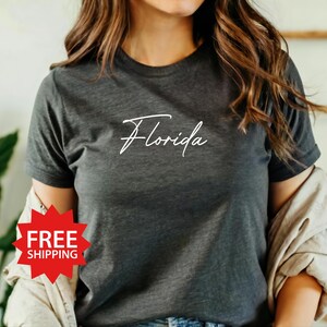 May include: A dark gray t-shirt with the word "Florida" written in white cursive script.