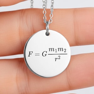 May include: A silver-toned circular pendant necklace featuring the black engraved physics formula for universal gravitation, F equals G times m1 times m2 divided by r squared, suspended from a delicate matching silver-toned metal chain.