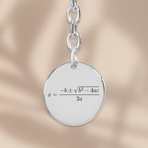 May include: A silver-coloured keyring with a circular pendant. The pendant displays a mathematical formula in black text. The keyring has a chain link and a ring for keys. The background is a soft, neutral colour.
