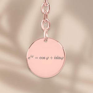 Könnte beinhalten: Roségoldener Schlüsselanhänger mit rundem Anhänger. Der Anhänger trägt die Gleichung e^(iφ) = cos φ + i sin φ. Der Schlüsselanhänger enthält eine Kette und einen runden Ring zur Befestigung.