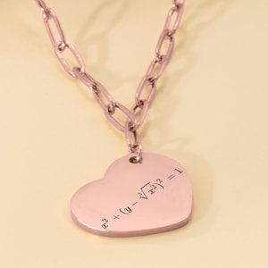 May include: A rose gold necklace with a heart-shaped pendant. The pendant has a mathematical equation engraved on it: "x^2 + (y - ^3√x^2)^2 = 1".