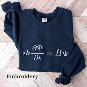 May include: A navy blue sweatshirt with the Schrödinger equation embroidered on the front in white. The equation reads "ih d/dt = H^ Psi".
