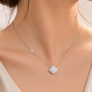 May include: A silver-toned necklace featuring a central four-leaf clover pendant encrusted with clear, sparkling stones. A smaller, matching four-leaf clover accent is positioned along the delicate chain to the side of the main pendant.
