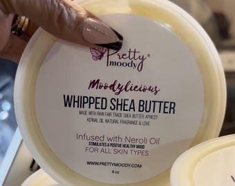 May include: A white jar with a pink and purple label that reads "Pretty Moody" and "Moodylicious Whipped Shea Butter". The label also says "Made with raw fair trade shea butter, apricot kernel oil, natural fragrance & love" and "Infused with Neroli Oil. Stimulates a positive healthy mood. For all skin types." The jar is 8 oz and has a website address printed on the label.