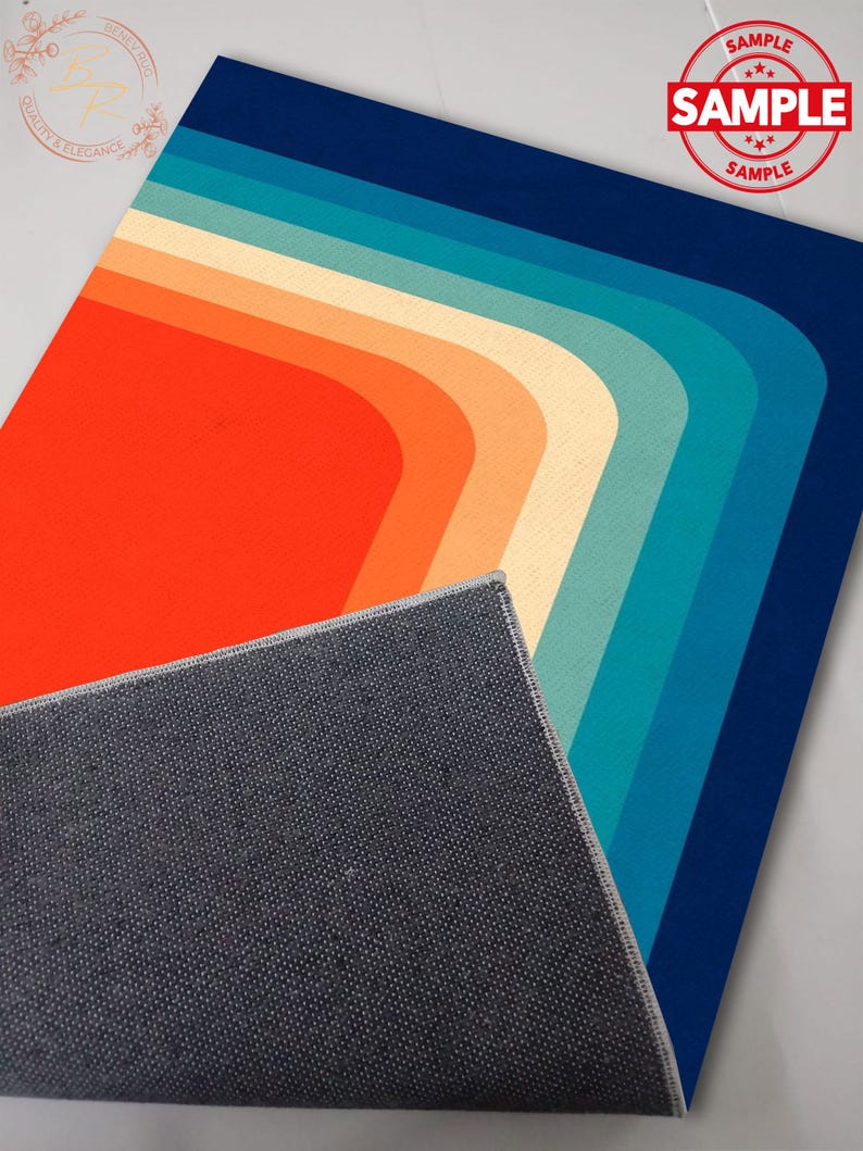May include: A retro-style rug with a vibrant color palette. The design features a series of curved stripes in shades of orange, cream, teal, and blue. The rug's edge is visible, revealing a gray backing. A "SAMPLE" stamp is in the upper right corner.