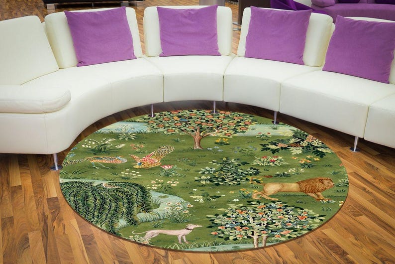 May include: A round area rug with a detailed pastoral scene. The rug features a green background with trees, flowers, and various animals, including a lion and a dog. The rug is placed on a hardwood floor.