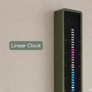 Peut inclure: Une horloge linéaire verticale avec un cadre vert olive et un panneau d'affichage noir. L'écran présente une colonne de segments lumineux de couleurs blanche, rose et bleue. Le texte "Linear Clock" apparaît à gauche et "@Curated3D" en bas.