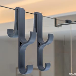 Puede incluir: Dos ganchos de plástico gris con un diseño de gancho doble, colgados de un alambre.