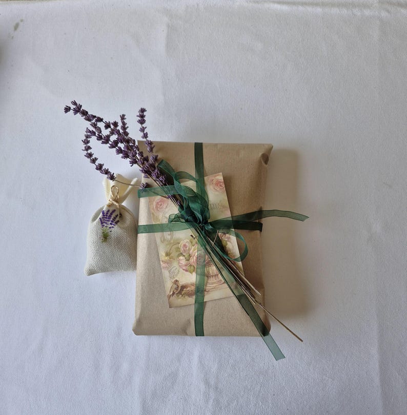Op de afbeelding: Een bruine papieren cadeauverpakking, gebonden met een groen lint en versierd met een vintage bloemenkaart en een klein lavendelzakje.
