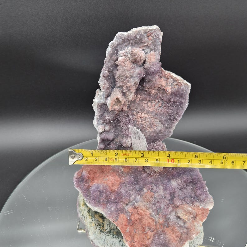 May include: A large, natural amethyst crystal cluster. The crystal features a mix of purple and pink hues, with a rough, textured surface. The crystal measures approximately 6 inches in length.