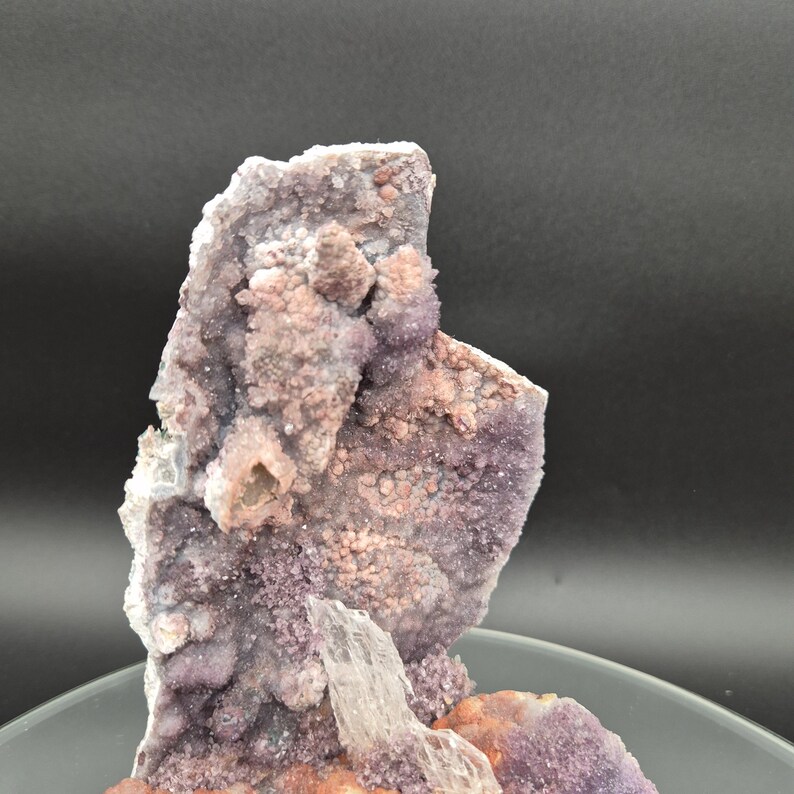 May include: A close-up of a natural amethyst geode with a crystalline structure. The geode features a mix of purple, pink, and white hues, with a rough, textured surface. The crystal formation is visible, showcasing the natural beauty of the mineral.