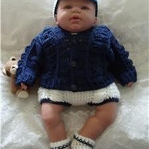 May include: A blue knitted baby cardigan with white buttons, a white knitted hat, and white knitted booties with black trim.