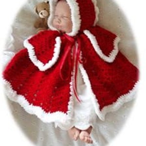 Puede incluir: Capa de bebé de ganchillo roja con ribete blanco y un lazo rojo. La capa tiene capucha y está hecha con un punto de encaje.