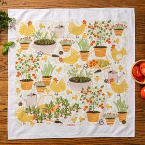 May include: White kitchen towel with a garden-themed design. The pattern includes yellow chickens, tomato plants, potted flowers, watering cans, and gardening tools. The towel has a border of green foliage and the word "GINGIBER" is printed on the bottom.