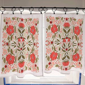May include: Two white kitchen curtains with a floral pattern. The design features large red flowers, smaller pink flowers, green leaves, and ladybugs. The curtains are hanging from a black rod with rings.