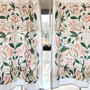 May include: White curtains with a repeating pattern of green hummingbirds, pink flowers, and green leaves. The design is set against a cream-colored background. The curtains are hanging from a gold-colored rod.