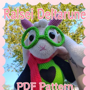 May include: A handmade crochet plushie of Ralsei from Deltarune, wearing green glasses, a red scarf, and a green and black outfit. The text "Ralsei Deltarune" and "PDF Pattern" are displayed in pink and white.