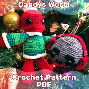 May include: A crochet pattern PDF showing two handmade dolls. One doll is red, green, and white, with black button eyes. The other is grey with red accents. The text "Bobette and Coal Dandys World" and "Crochet Pattern PDF" are displayed.