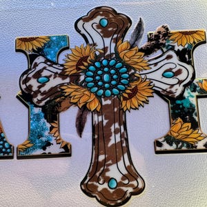 May include: A decorative cross with a cowhide pattern, turquoise accents, and sunflower details. The cross features a central turquoise stone design and is adorned with feathers. The overall design has a rustic, country aesthetic.