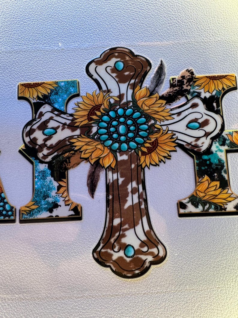 May include: A decorative cross with a cowhide pattern, turquoise accents, and sunflower details. The cross features a central turquoise stone design and is adorned with feathers. The overall design has a rustic, country aesthetic.
