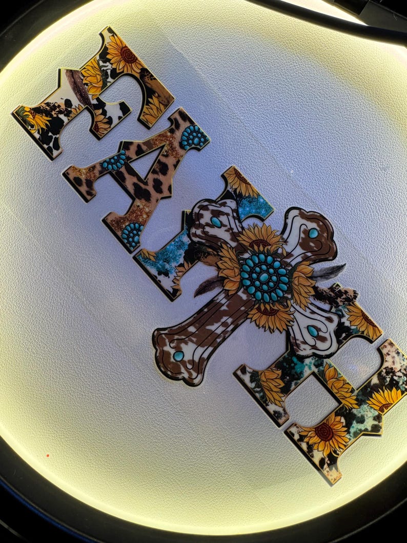 May include: Wooden cut-out letters spelling "FAITH" with a cross-shaped "H". The letters and cross feature a mix of patterns: cowhide, leopard print, sunflowers, and turquoise accents. The design has a rustic, country aesthetic.