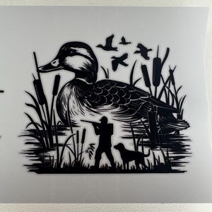May include: Black and white silhouette of a duck in a marsh setting. The image includes a hunter aiming a rifle, a dog, flying birds, and cattails. The duck is the central focus, with detailed feather patterns.