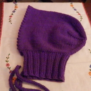 May include: Purple knitted hooded hat with a long tie. The hat is made of a soft, textured yarn and has a simple, classic design.