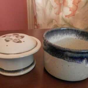 May include: A white ceramic butter dish with a lid. The lid has a brown and white design with a raised pattern. The dish has a blue and white glaze with a speckled finish.
