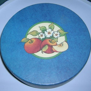 May include: A blue round box with a white and green circle design featuring three red apples and white flowers.